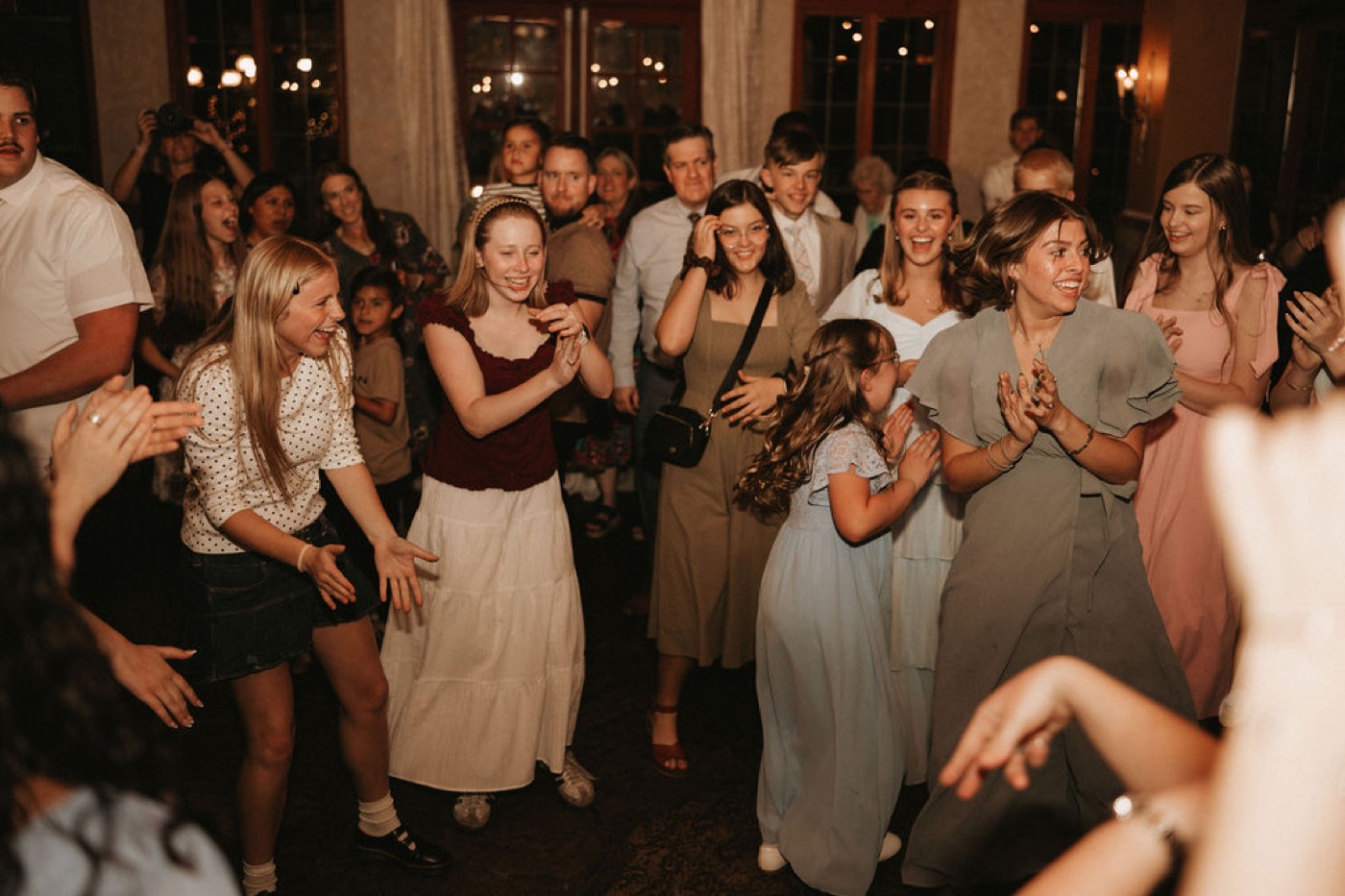 Packed dance floor at a wedding reception with guests clapping and dancing