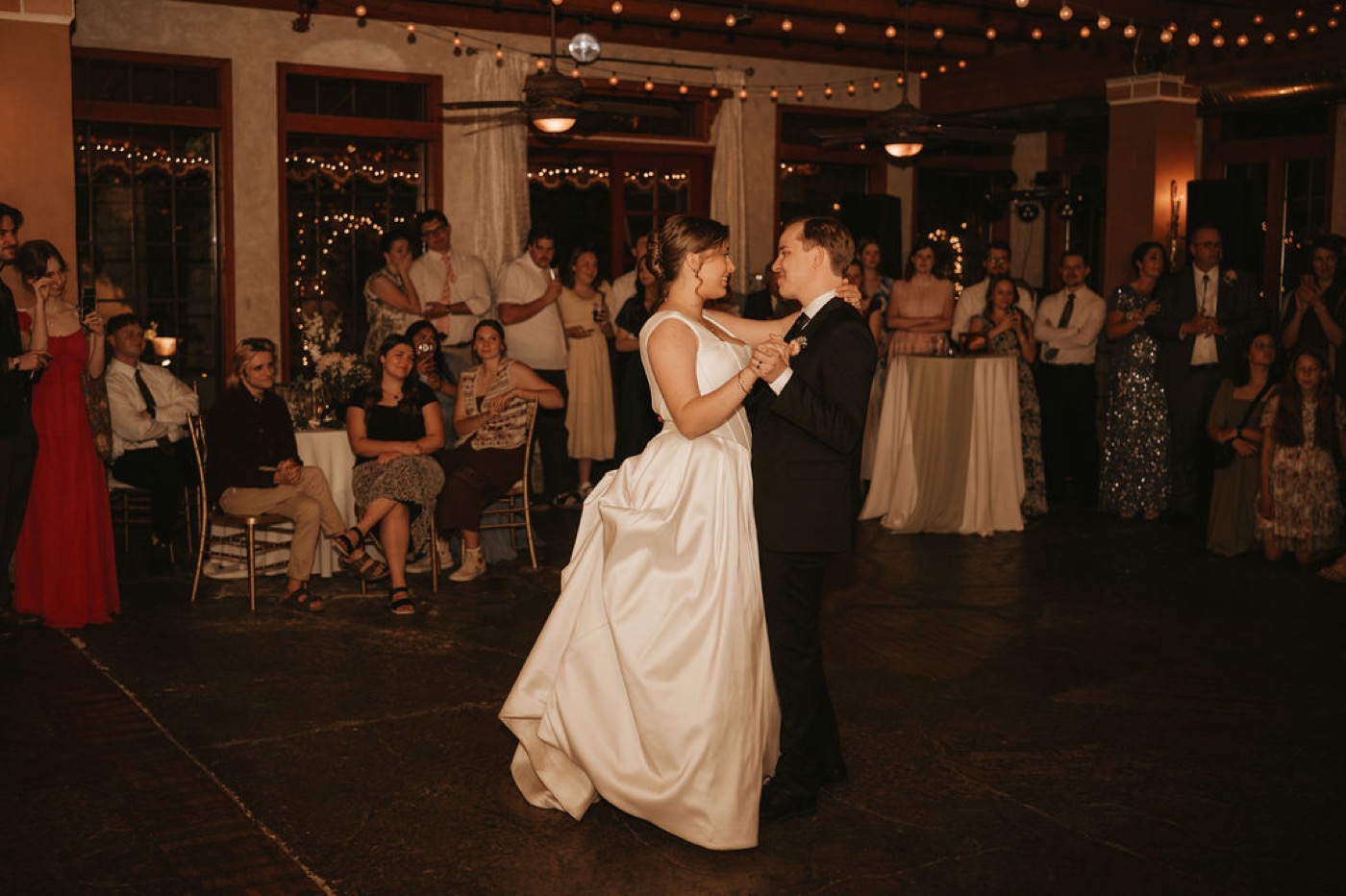 Bride and groom first dance with string lights and guests watching
